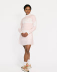 A woman wearing a pink fore all Fore Sweater with white accents and a green skirt.