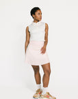 Woman wearing a white sleeveless Moore Polo and light pink skirt on a white background
