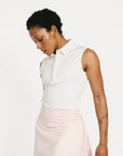 Woman wearing a white sleeveless Moore Polo and light pink skirt on a white background
