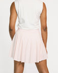 Person wearing a white sleeveless top and light pink skirt on a white background