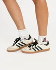 White sneakers with black stripes and 'A' logo worn with white socks on a light background