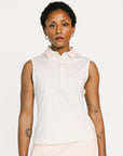 Woman wearing a white sleeveless Moore Polo and light pink skirt on a white background