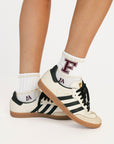 White sneakers with black stripes and 'F' logo worn with white socks on a light background
