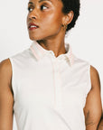 Woman wearing a white sleeveless Moore Polo and light pink skirt on a white background
