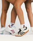 Two pairs of legs wearing colorful socks with letter designs and sneakers on a white background.