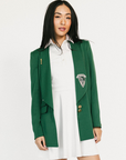 Woman wearing a green blazer with a logo over a white dress on a white background