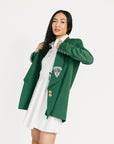 Woman wearing a green blazer over a white dress with a logo on a white background