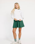 Woman wearing a white Dorothy sweater with green accents and a green skirt on a white background