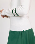 Woman wearing a white Dorothy sweater with green accents and a green skirt on a white background