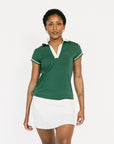 Woman wearing a green and white polo shirt with a white skirt on a white background