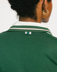 Woman wearing a green polo shirt with white trim on a white background