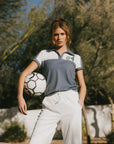 A woman wearing a color block indigo polo shirt with front and back yoke detailing, paired with white pants.