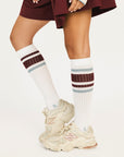 White knee-high socks with red and blue stripes worn with beige sneakers on a white background