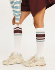 White knee-high socks with maroon and gray stripes worn with beige sneakers on a light background