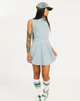Woman wearing a light blue sleeveless dress with a logo and a matching cap on a white background