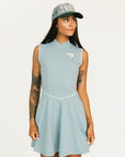 Woman wearing a light blue sleeveless dress with a logo and a matching cap on a white background