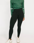 Person wearing a green long-sleeve top and black leggings on a white background