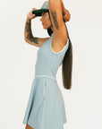 Woman wearing a light blue sleeveless dress with a logo and a matching cap on a white background