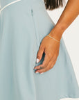 Light blue dress with a hand adjusting the waistband on a white background