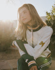 A model wearing the vonn half zip in white sitting on a bench with plants in the background.