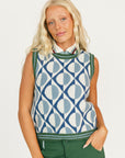 Woman wearing a patterned sleeveless sweater and green pants on a white background
