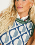 Woman wearing a patterned sleeveless sweater and green pants on a white background