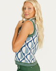 Woman wearing a patterned sleeveless sweater and green pants on a white background