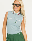 Woman wearing a sleeveless light blue golf polo shirt with a logo and green pants on a white background