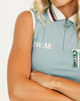 Woman wearing a sleeveless light blue golf polo shirt with a logo and green pants on a white background