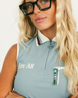 Woman wearing a sleeveless light blue golf polo shirt with a logo and green pants on a white background