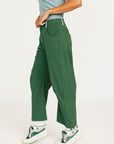 Person wearing green pants and white sneakers on a light gray background