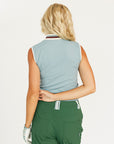 Woman wearing a sleeveless light blue golf polo shirt with a logo and green pants on a white background