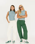 Two women wearing sleeveless tops and pants standing against a white background