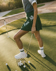 A person wearing a green skirt with a mesh back, paired with a blue top and green sneakers. The skirt has a high waist and a mid-thigh length cut.
