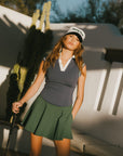 A woman wearing a sleeveless indigo blue polo with a striped collar and v-neck.