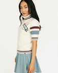 Woman wearing a Macbeth Turtleneck sweater, light blue skirt, and white sneakers on a white background