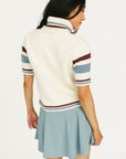 Woman wearing a Macbeth Turtleneck sweater, light blue skirt, and white sneakers on a white background