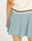 Woman wearing a Macbeth Turtleneck sweater, light blue skirt, and white sneakers on a white background