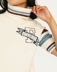 Woman wearing a Macbeth Turtleneck sweater, light blue skirt, and white sneakers on a white background
