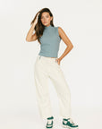 Woman wearing a light blue sleeveless top and white pants with green sneakers on a white background