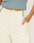 Person wearing a light blue top and cream-colored pants on a plain background