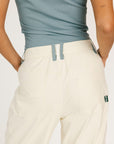 Person wearing a light blue sleeveless top and beige pants on a plain background