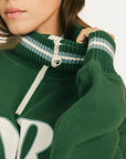 Green sweater with white zipper and lettering on a neutral background