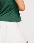 Woman wearing a green sleeveless Moore Polo shirt with white trim on a plain background