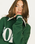 Person wearing a green sweatshirt with white lettering on a plain background