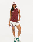 Woman wearing a maroon sleeveless polo shirt and cap with white accents, standing against a plain background.
