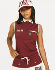 Woman wearing a maroon sleeveless polo shirt and cap with white accents, standing against a plain background.