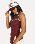 Woman wearing a maroon sleeveless polo shirt and cap with white accents, standing against a plain background.