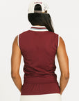 Woman wearing a maroon sleeveless polo shirt and cap with white accents, standing against a plain background.