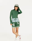 Person wearing a green Marie long-sleeve shirt and light blue shorts with a cap on a white background